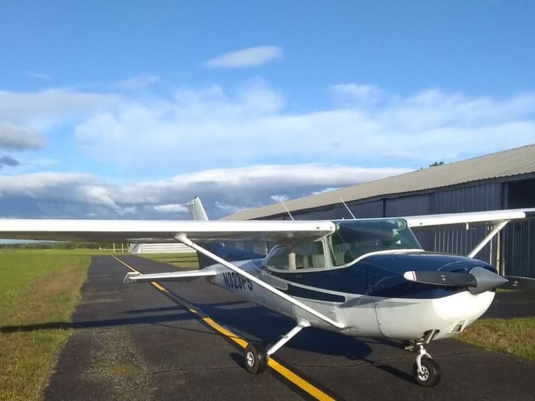 A white-and-navy Cessna 172 Skyhawk parked on the taxiway beside a hangar row, its registration N323FS on the fuselage.